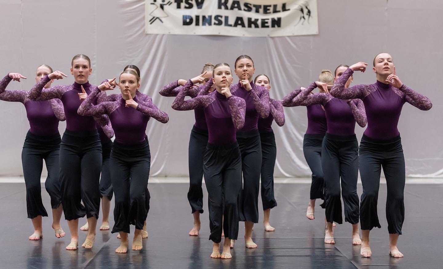 Große Tanzformation in lila Oberteilen und schwarzen Hosen auf der Bühne