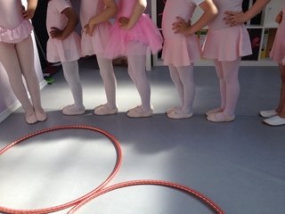 Kinder in rosa Trikots und Ballettschläppchen stehen in einer Reihe hinter zwei Reifen