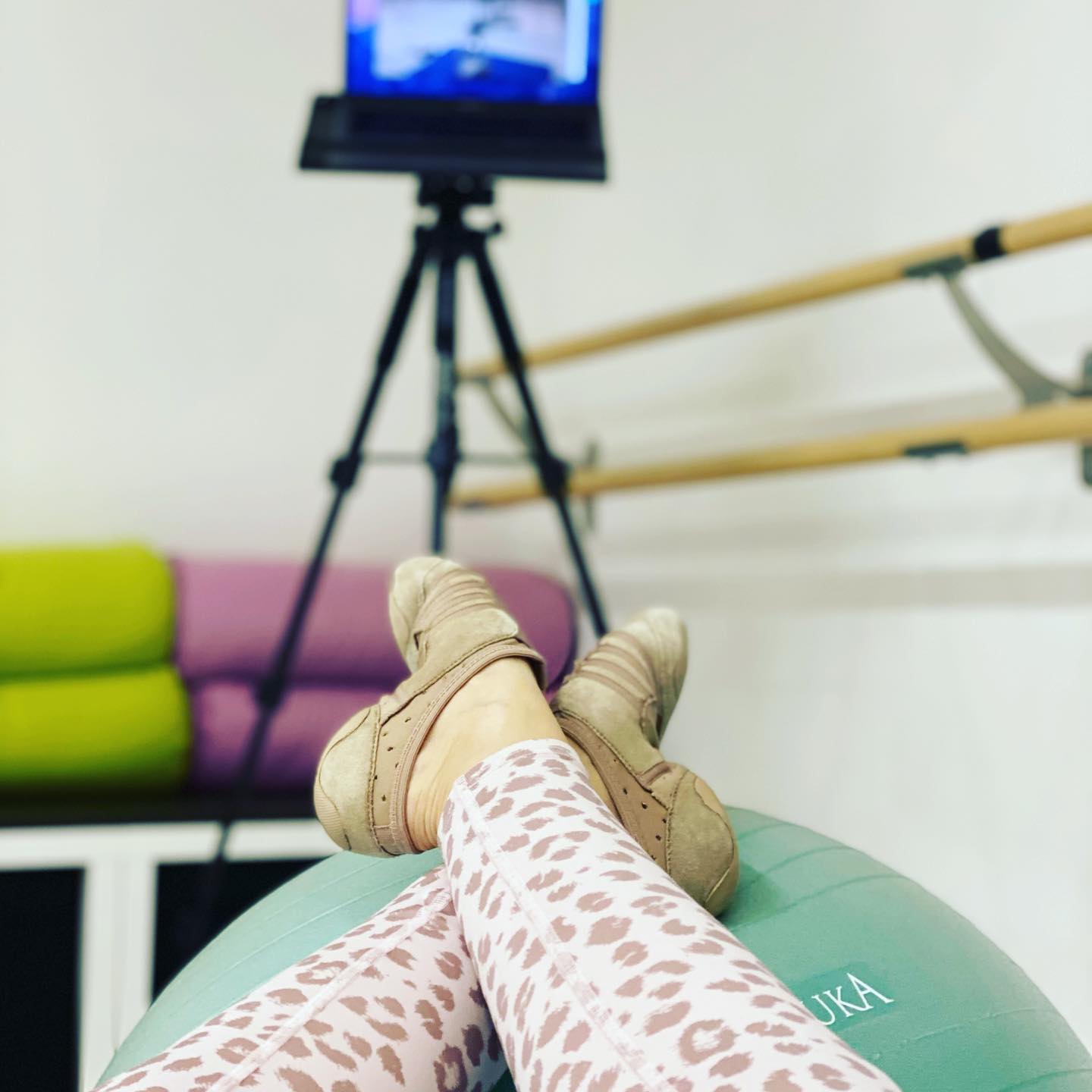Füße in Tanzschuhen auf einem Gymnastikball vor einer Ballettstange