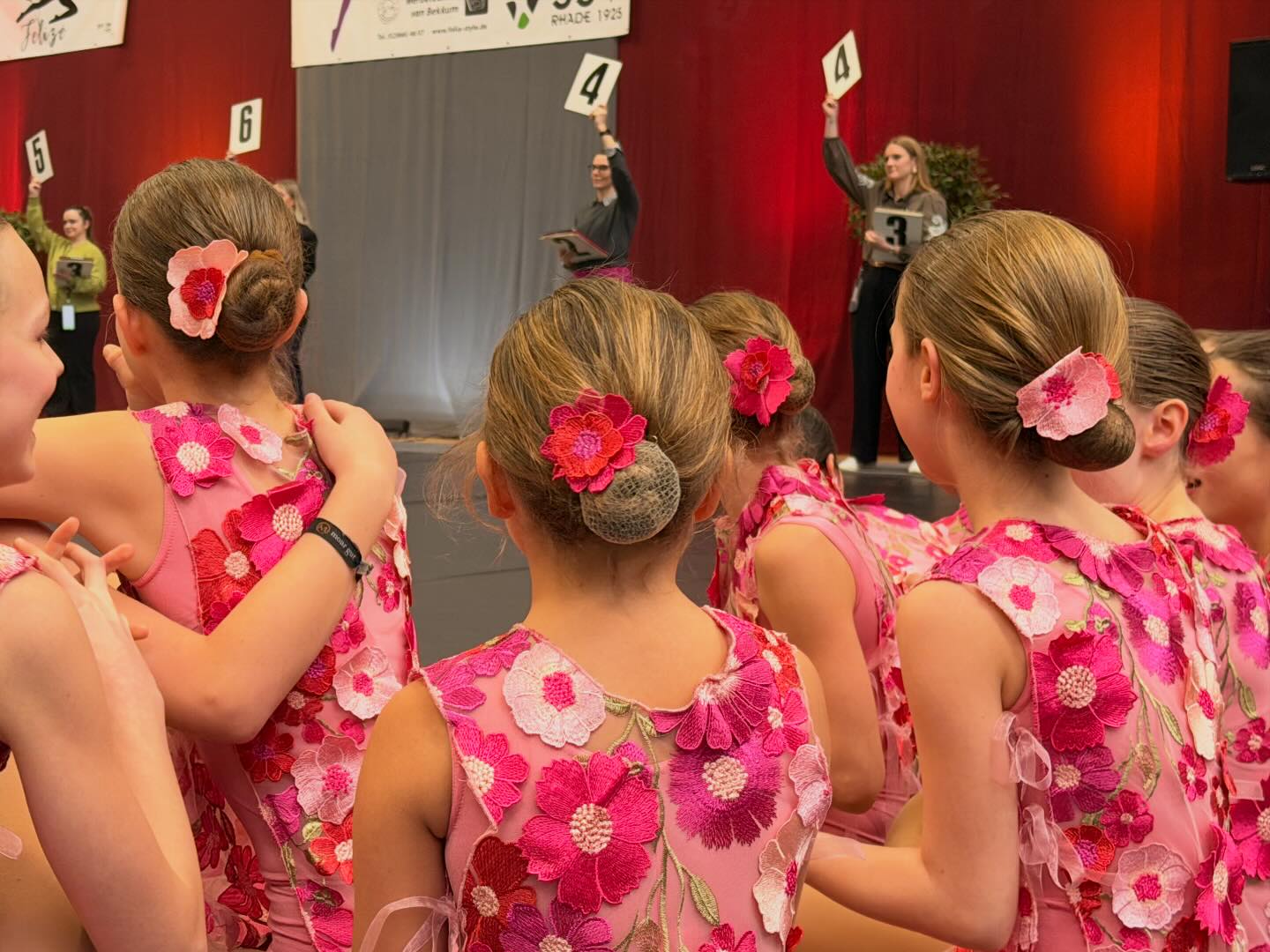 Kinder in rosa Blumenkostümen von hinten, im Hintergrund Wertungsrichterinnen mit Punktetafeln